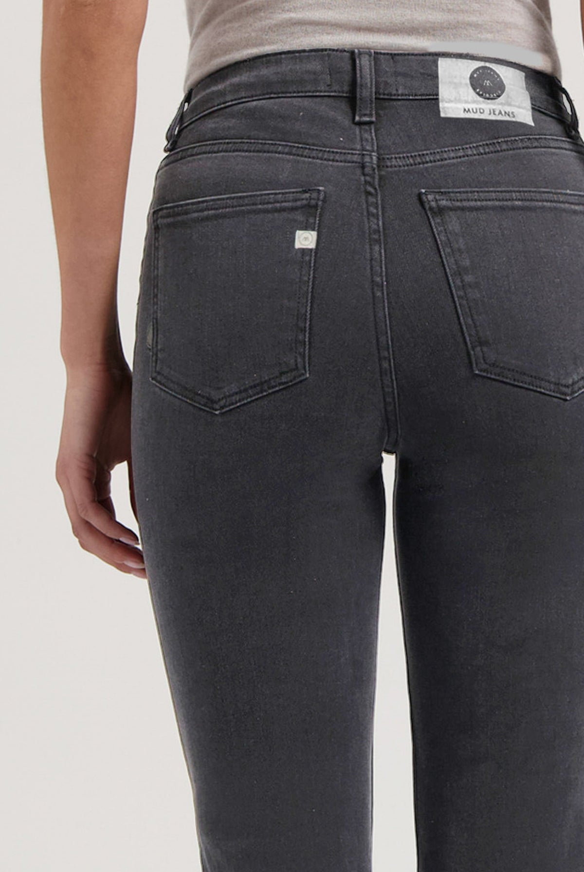 Close-up of dark gray MUD Jeans denim showcasing back pockets and sustainable fabric detail, worn with a light beige top.