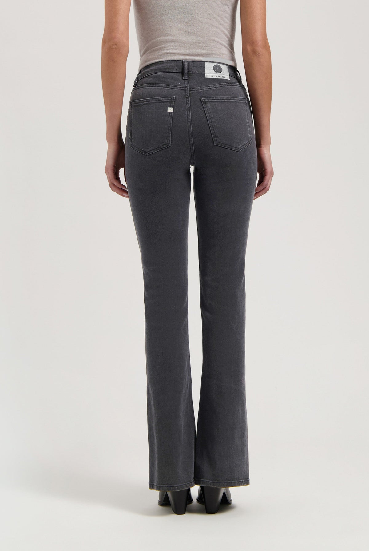 Back view of sustainable MUD Jeans in washed black, showcasing straight-leg fit, paired with a fitted beige top for modern style.