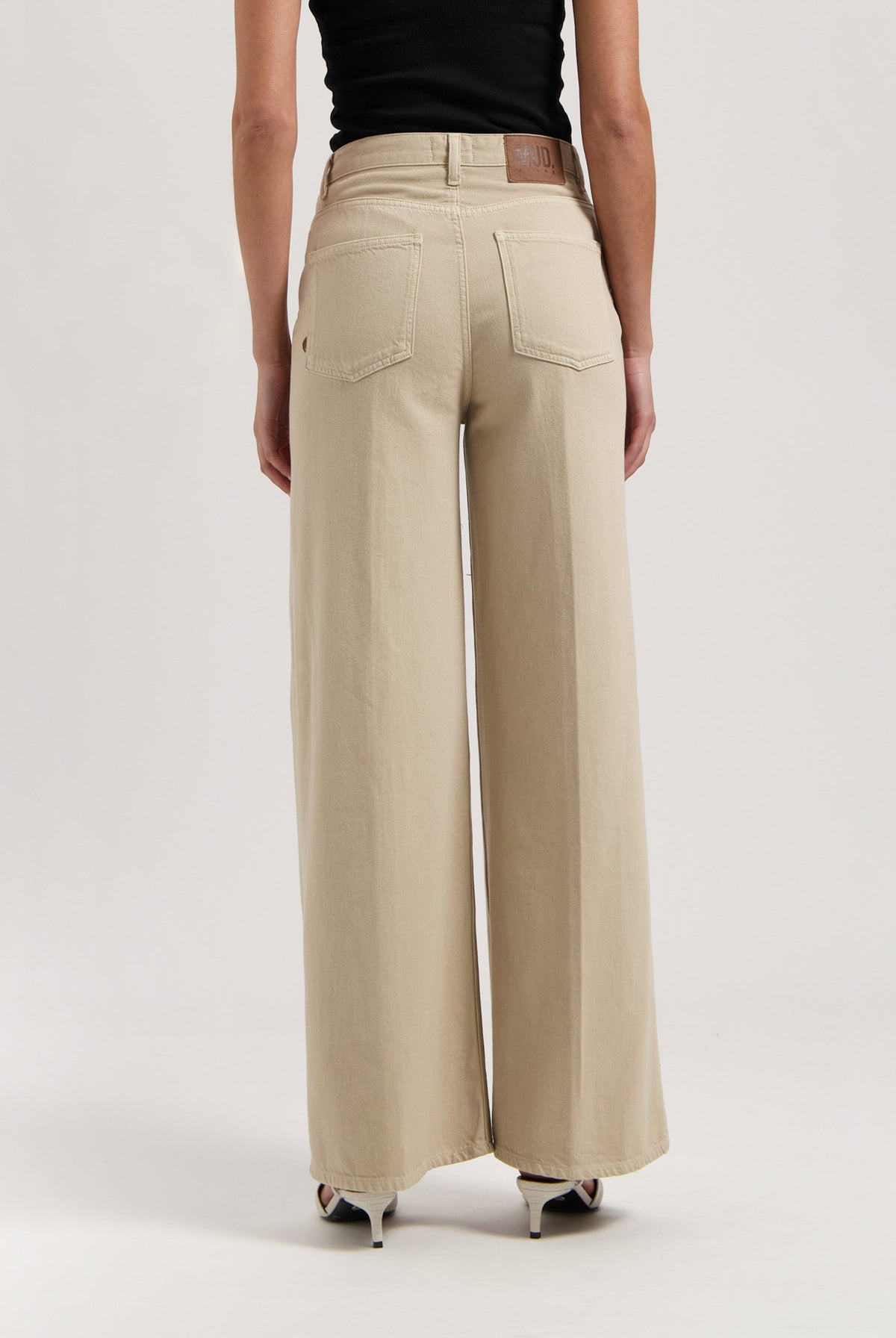 High-waisted beige wide-leg pants made from organic cotton, modeled with a black sleeveless top and white high heels.