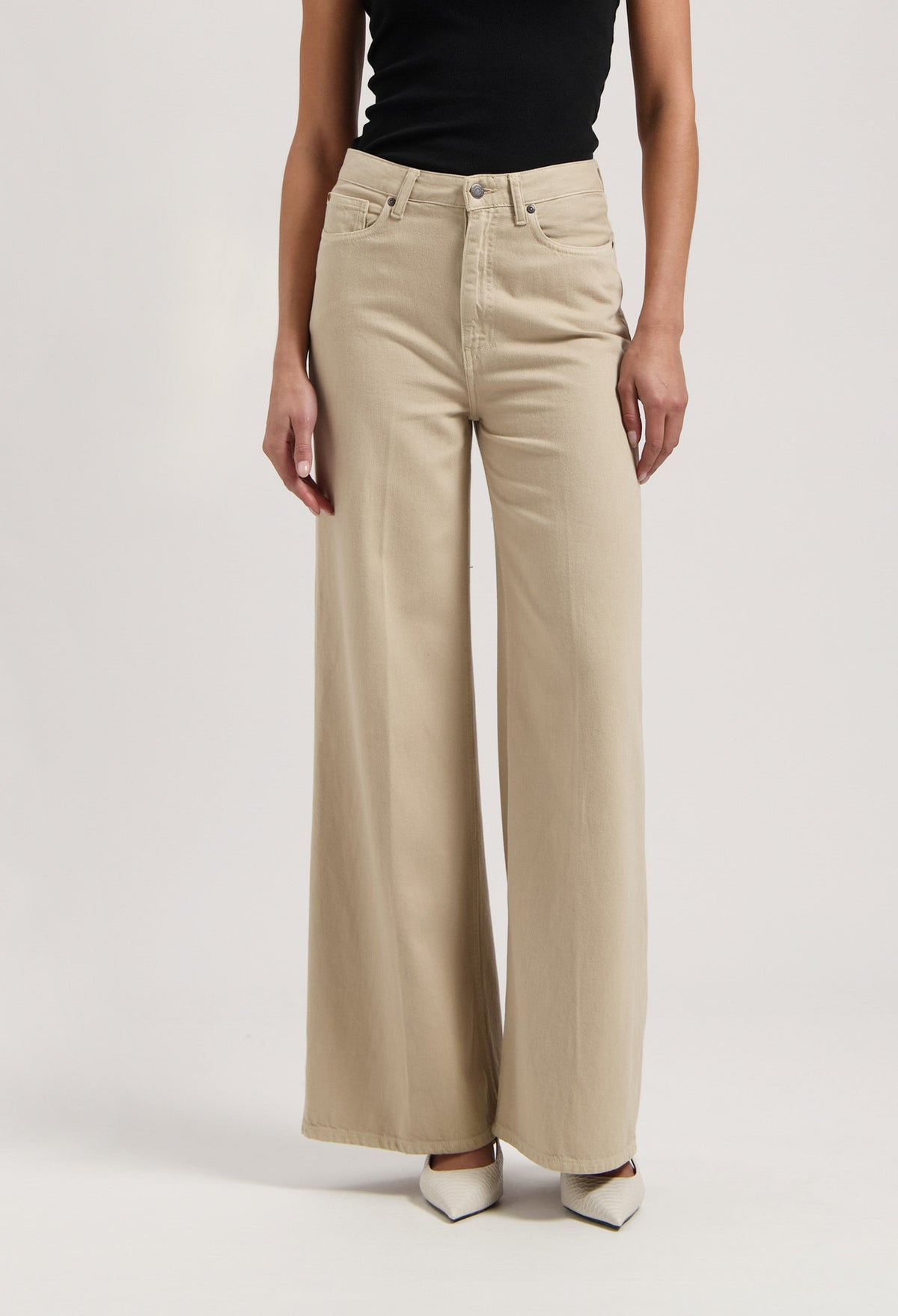 High-waisted wide-leg beige trousers made from soft fabric, worn with a black sleeveless top and white pointed shoes.