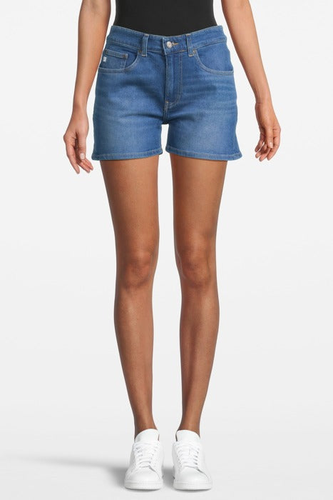 High-waisted blue denim shorts made from organic cotton, paired with a black top and white sneakers for a casual look.