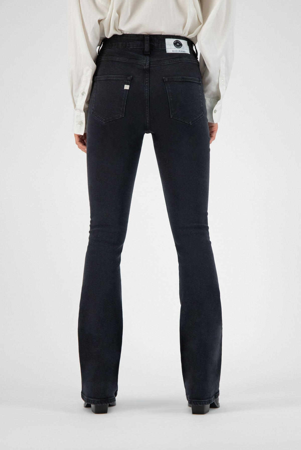 High-waisted black denim jeans by MUD, featuring a flattering fit, visible back pockets, worn with a classic white shirt.
