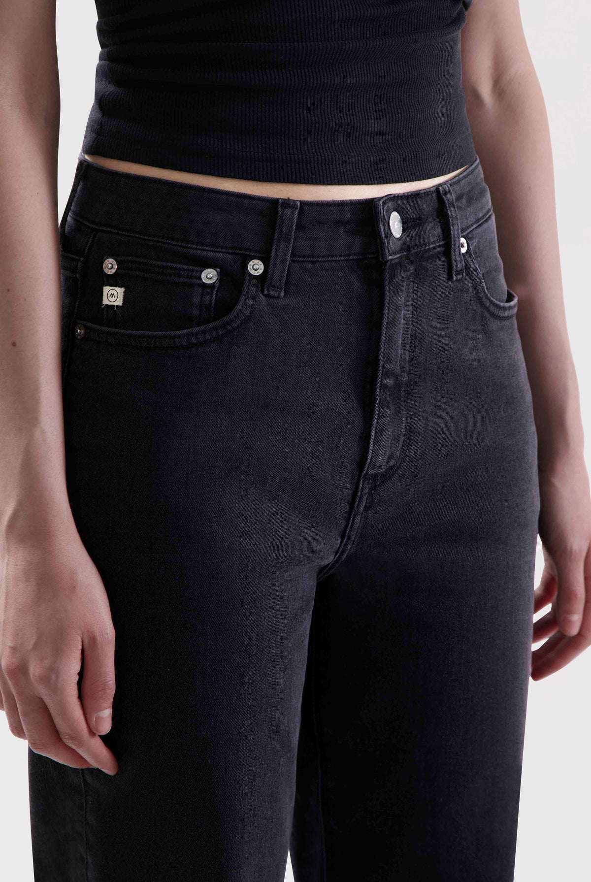 Black high-waisted jeans made from sustainable denim, worn with a sleeveless ribbed black top, close-up view.