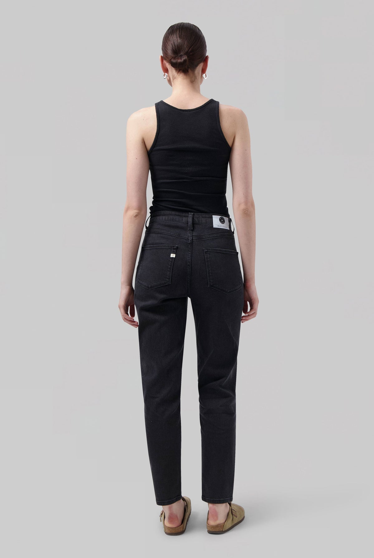 Woman wearing black ribbed tank top and charcoal straight-leg jeans with a back label, styled with tan slip-on shoes.