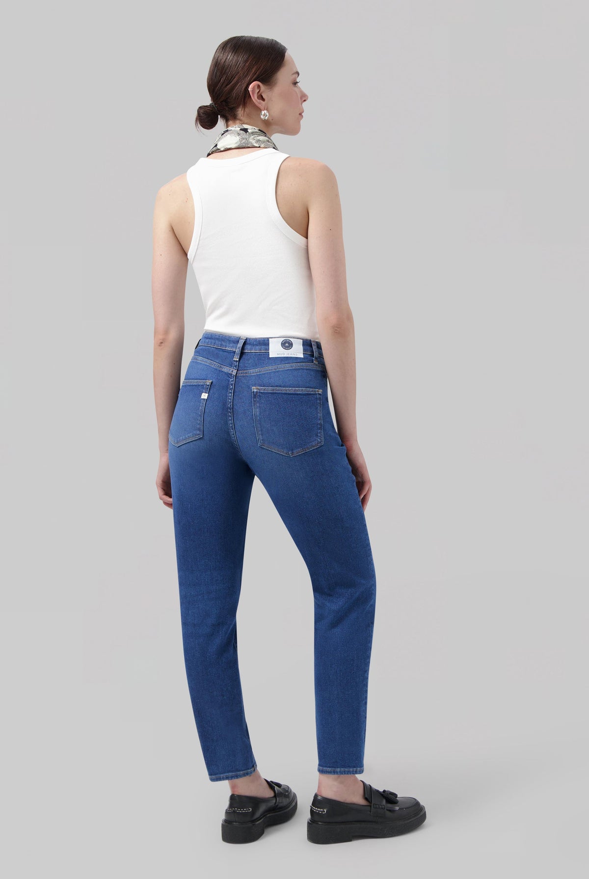 Casual blue denim jeans paired with a white sleeveless top and loafers, styled with a chic scarf accessory.