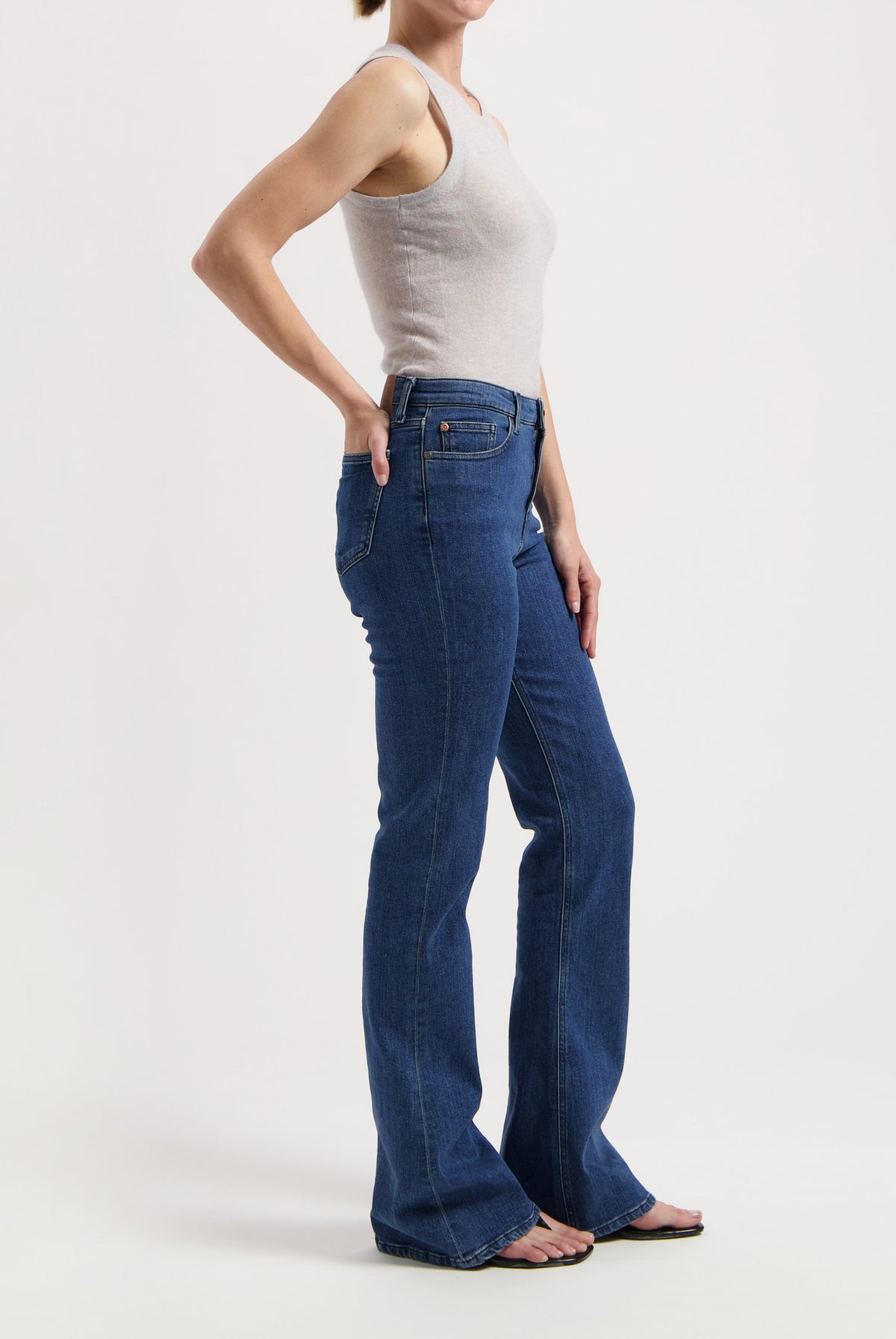 Model wearing a sleeveless beige top with blue high-waisted bootcut jeans, showcasing casual style and fit.