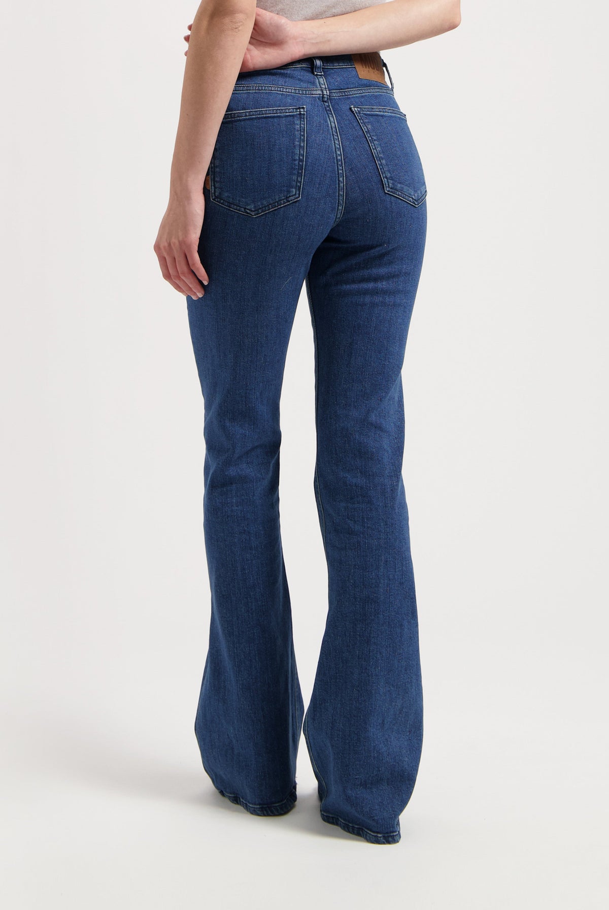 Woman wearing bootcut blue jeans made from eco-friendly denim, showcasing rear view details with pockets and seam stitching.