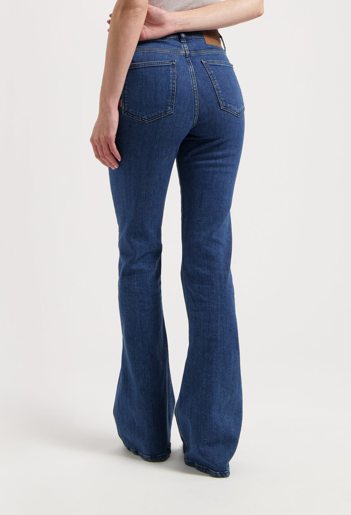 Woman wearing bootcut blue jeans made from eco-friendly denim, showcasing rear view details with pockets and seam stitching.
