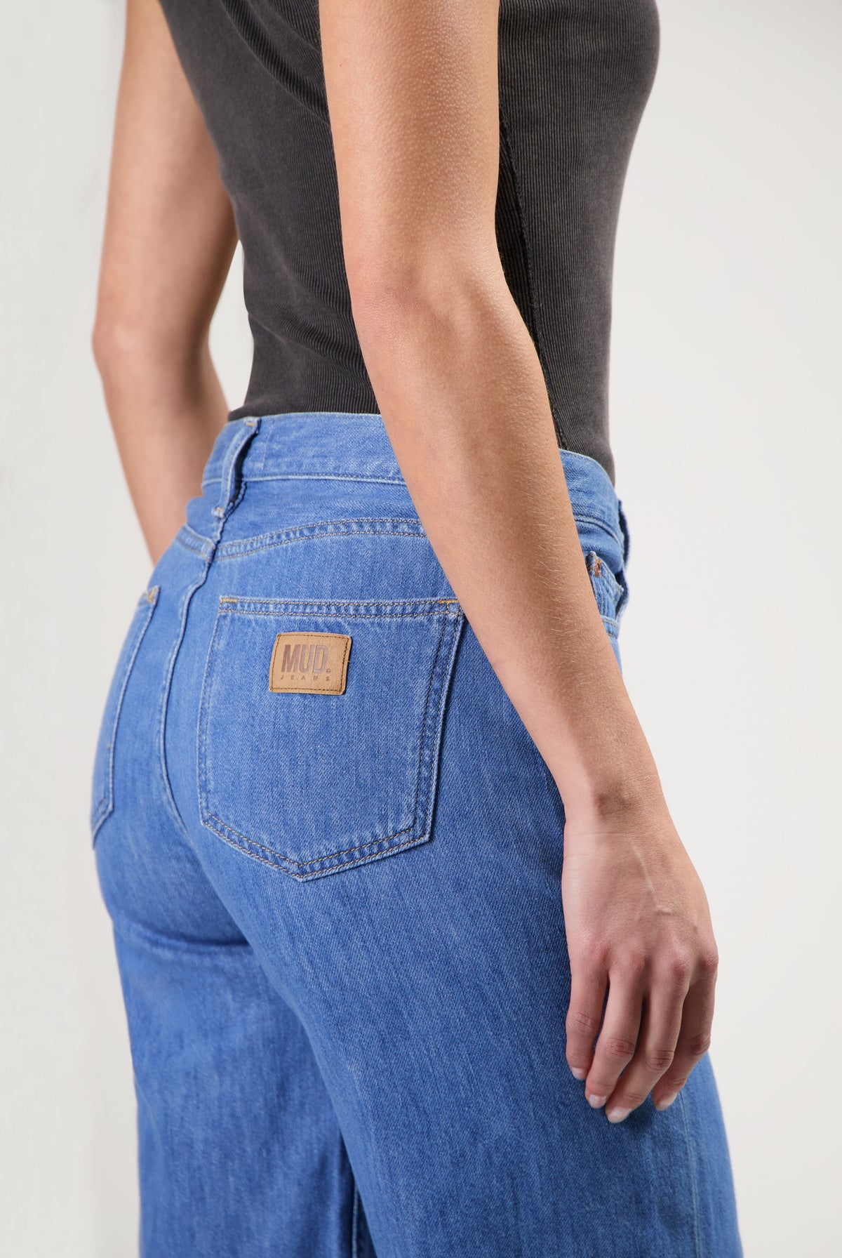 Close-up of MUD Jeans in blue denim, showcasing a high-waisted, relaxed fit style worn with a fitted black top.