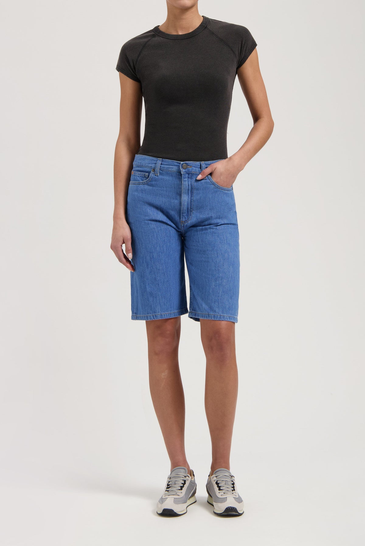Casual light blue denim Bermuda shorts paired with a fitted black tee and gray sneakers, showcasing a relaxed outfit.