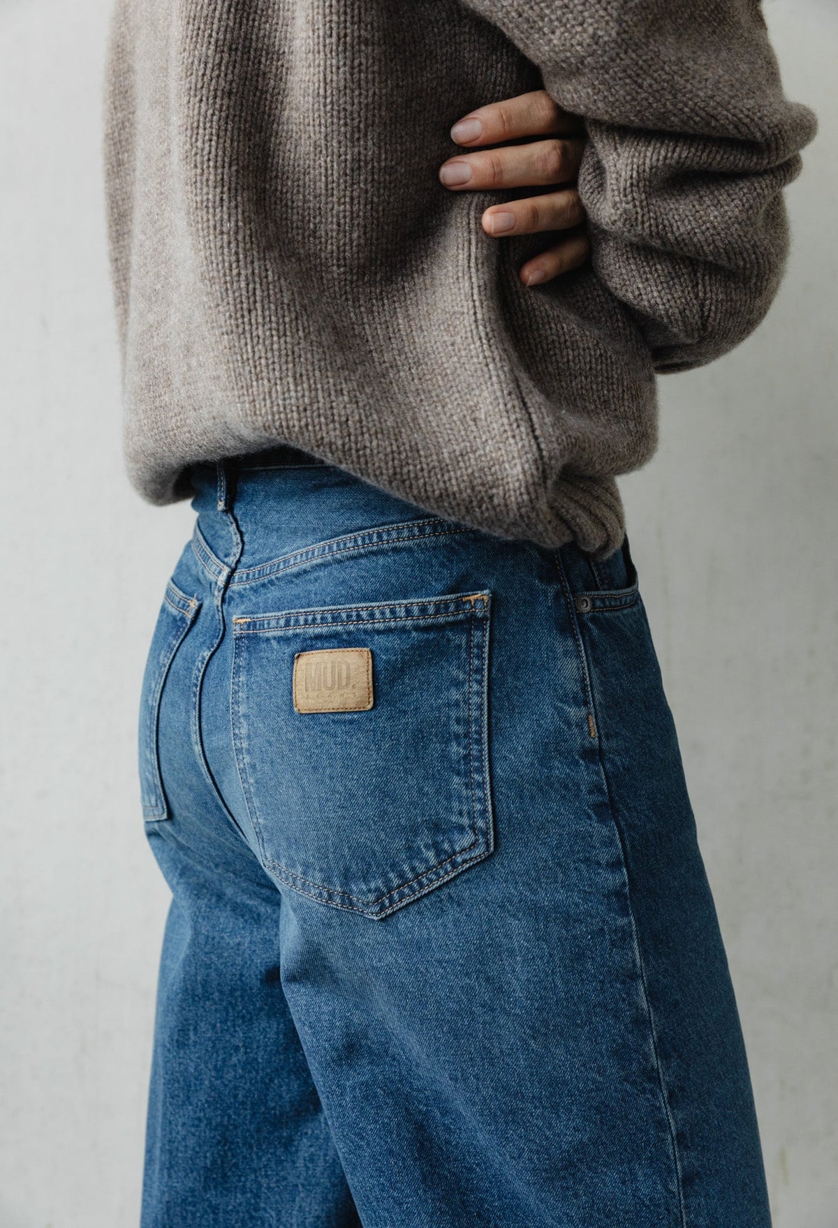 Person wearing blue MUD jeans paired with a cozy beige knitted sweater, showcasing a sustainable casual fashion look.