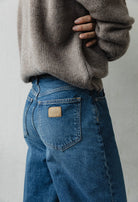 Person wearing blue MUD jeans paired with a cozy beige knitted sweater, showcasing a sustainable casual fashion look.