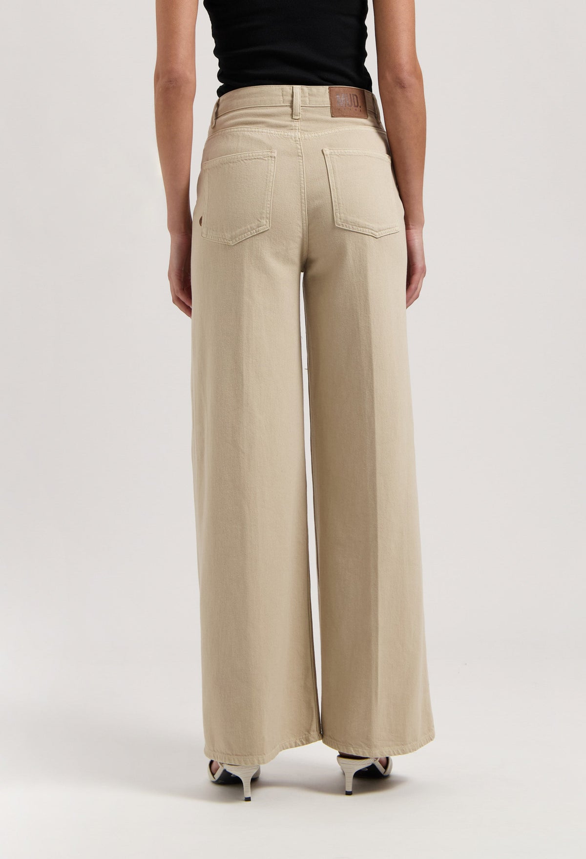 High-waisted beige wide-leg pants made from organic cotton, modeled with a black sleeveless top and white high heels.