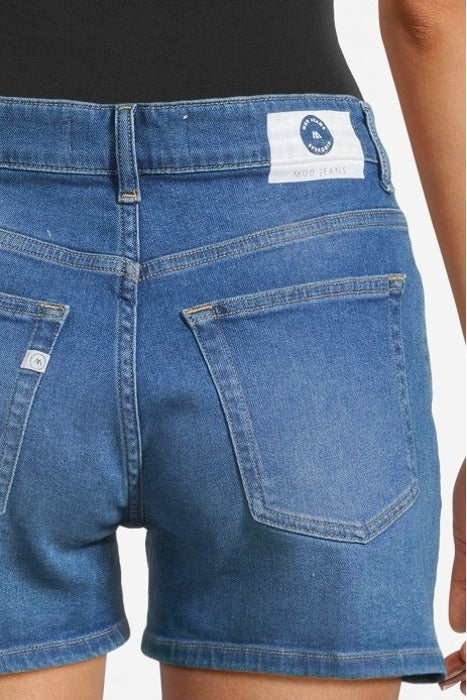 Blue denim MUD Jeans shorts worn with a black top, showcasing sustainable fashion with classic pocket stitching.