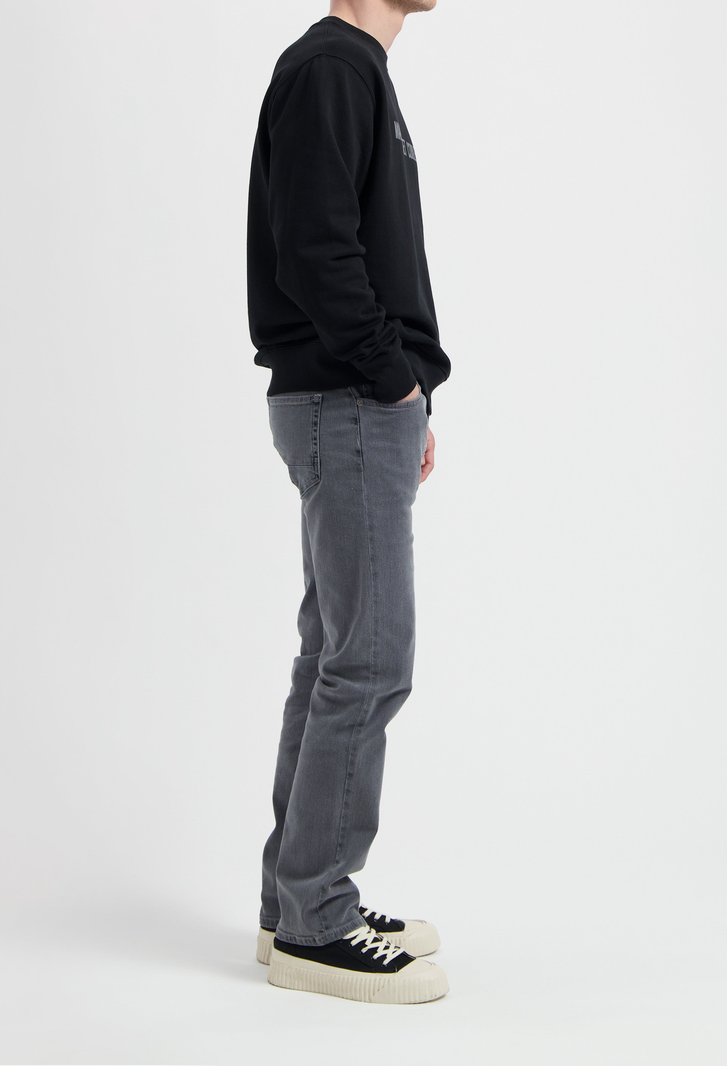 Sustainable MUD Jeans in gray denim, crafted ethically from organic cotton, paired with a black sweatshirt and sneakers.