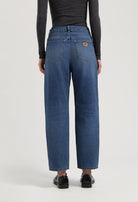 Loose-fit, mid-blue jeans by MUD Jeans made from organic cotton, styled with a dark long-sleeve top and black shoes.