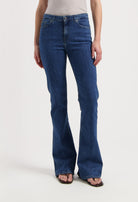 Woman wearing bootcut blue denim jeans, showcasing a classic fit, paired with a beige sleeveless top and flip-flops.