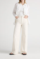 White wide-leg denim jeans paired with a tucked-in white tank top and unbuttoned shirt, worn with black sandals.