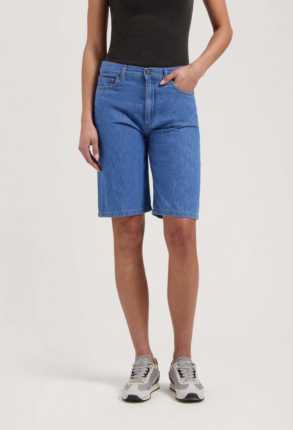 Casual blue denim bermuda shorts paired with a fitted black tank top and chic gray-white sneakers, showcasing a relaxed style.