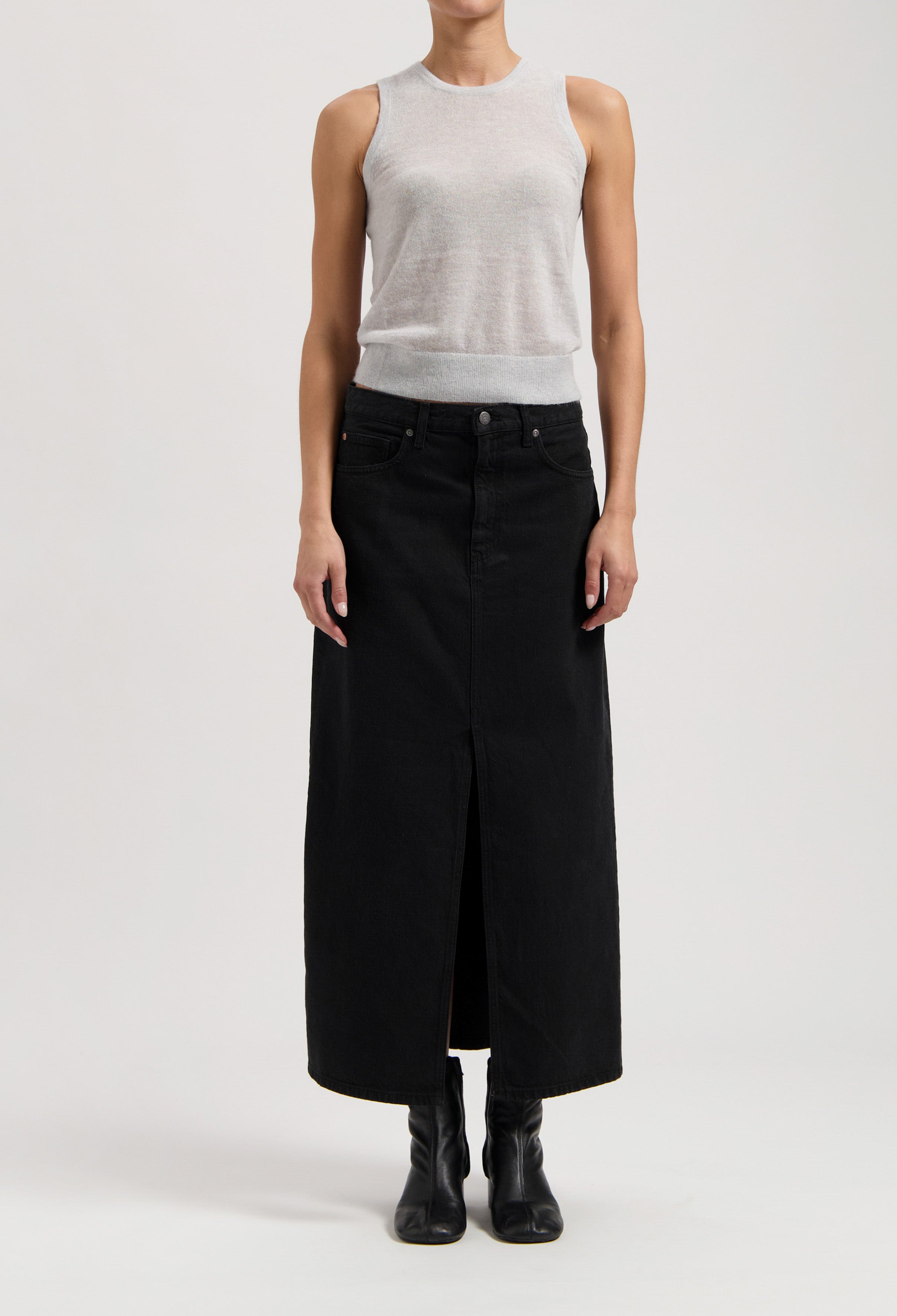 Model wearing a sleeveless gray top with a long black denim skirt, featuring a central slit, and black ankle boots.